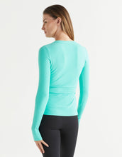 Person wearing a light blue long-sleeve top and black leggings on a white background
