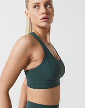 Woman wearing a green sports bra and leggings on a light gray background