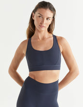 Woman wearing a navy blue sports bra and leggings on a white background