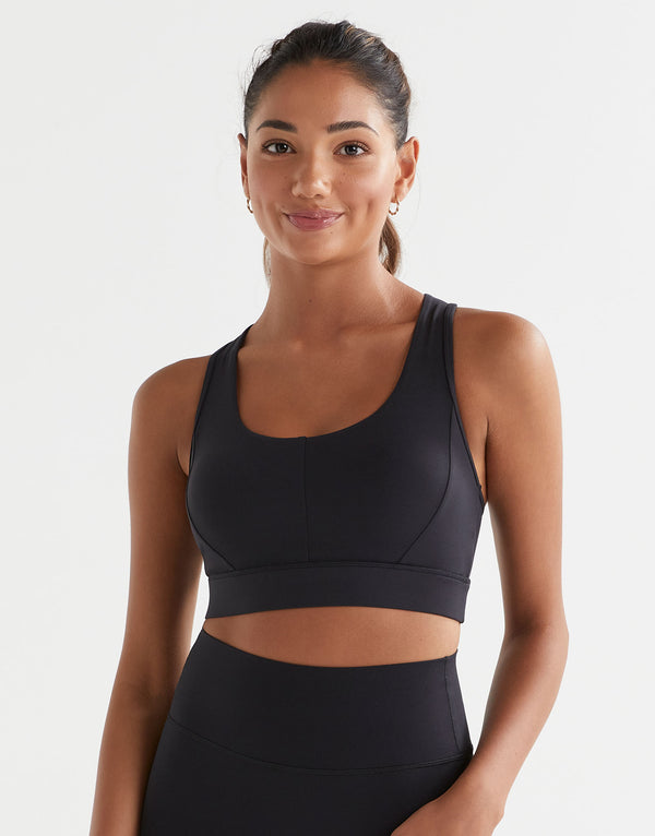 Woman wearing a black sports bra and leggings on a light gray background