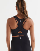 A woman wearing a black Lilybod Frankie Cloud-Core Sports Bra with wide straps and removable padded cups and black leggings.