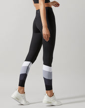 A woman wearing black color-block leggings with white and gray accents, posing with a side view.