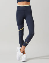 Navy leggings with yellow accents worn by a person on a gray background