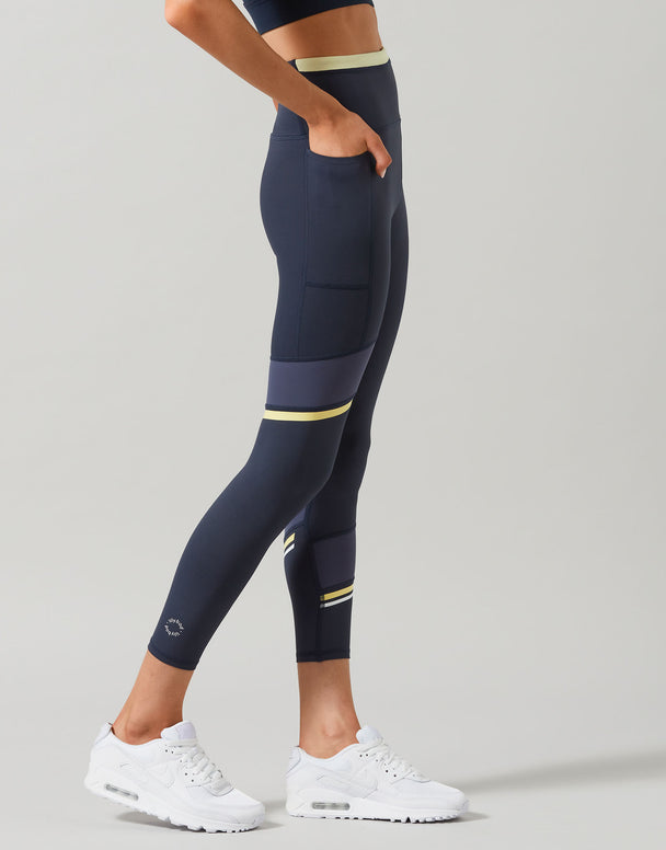 Person wearing navy leggings with yellow accents on a gray background