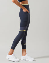 Person wearing navy leggings with yellow accents on a gray background