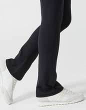 Black pants worn by a person with white sneakers on a light gray background