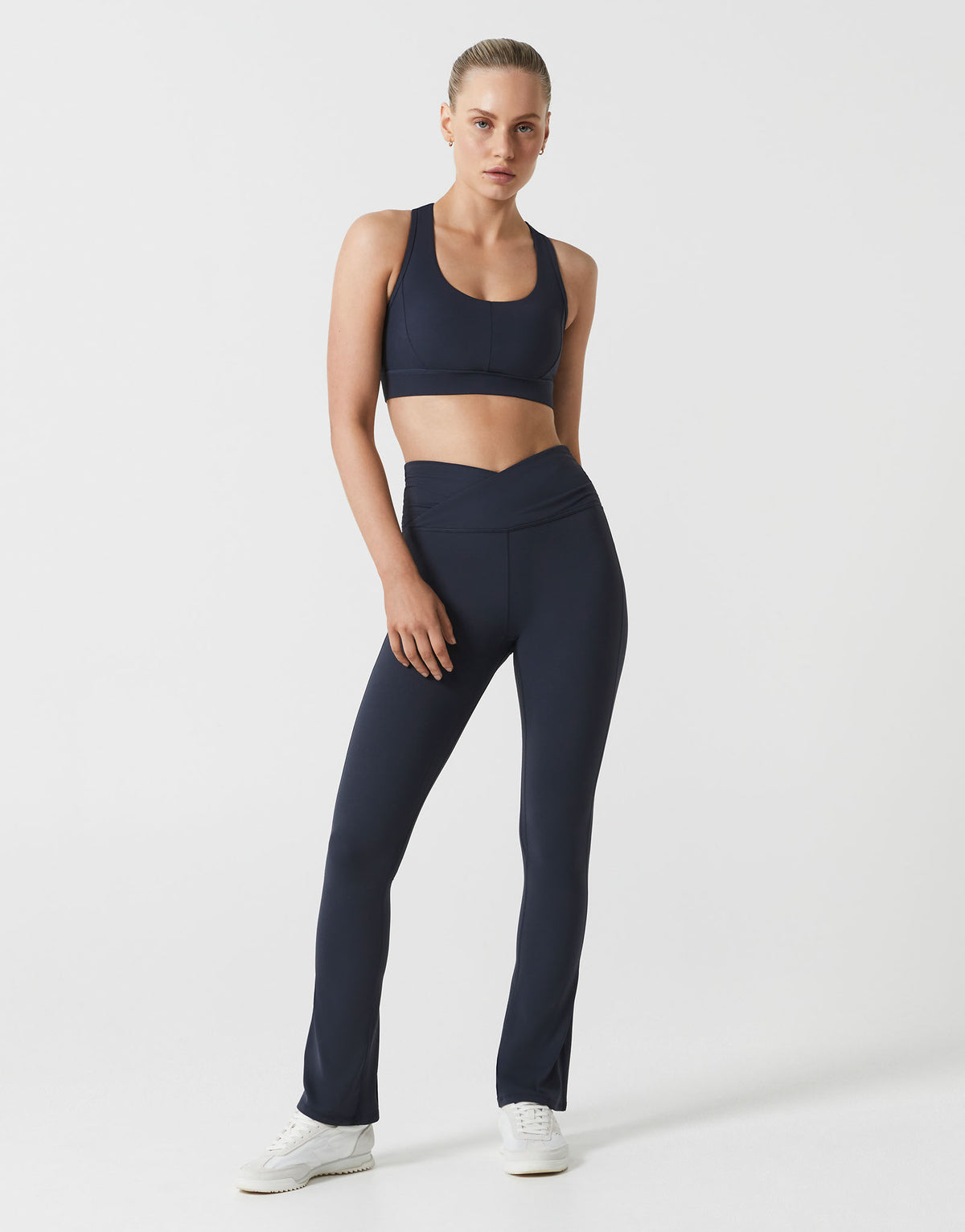A woman wearing navy bootleg leggings and w matching top on a white background.
