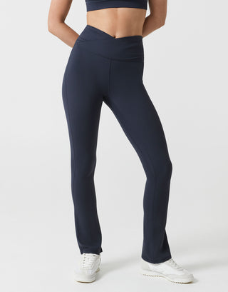 A woman wearing navy bootleg leggings with a v dipped waist on a white background.