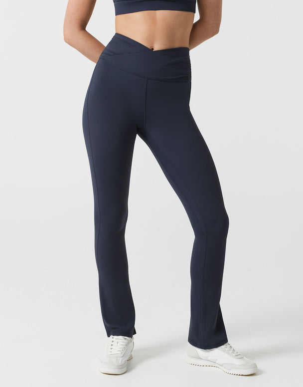 A woman wearing navy bootleg leggings with a v dipped waist on a white background.