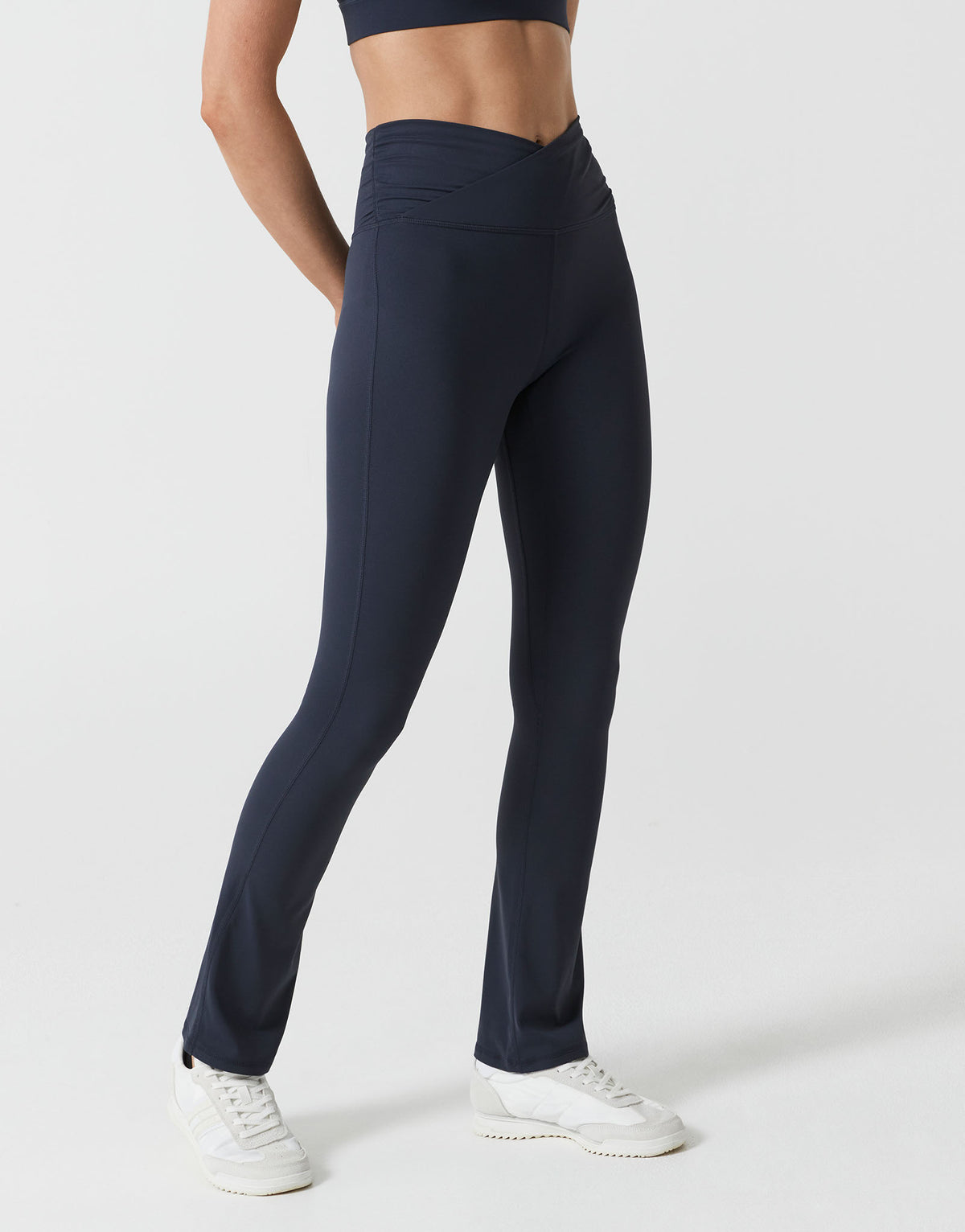 A woman wearing navy bootleg leggings with a v waist on a white background.