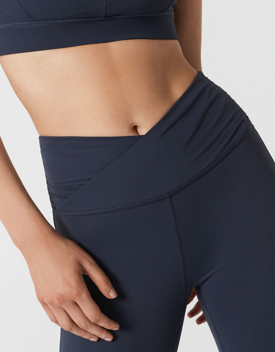 Close up of a woman wearing navy bootleg leggings on a white background.