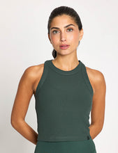 Woman wearing a green ribbed tank top against a plain background