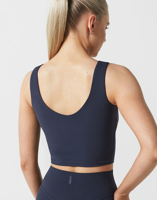 Woman wearing a navy blue sports bra and leggings on a light gray background