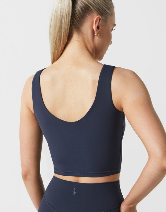 Woman wearing a navy blue sports bra and leggings on a light gray background