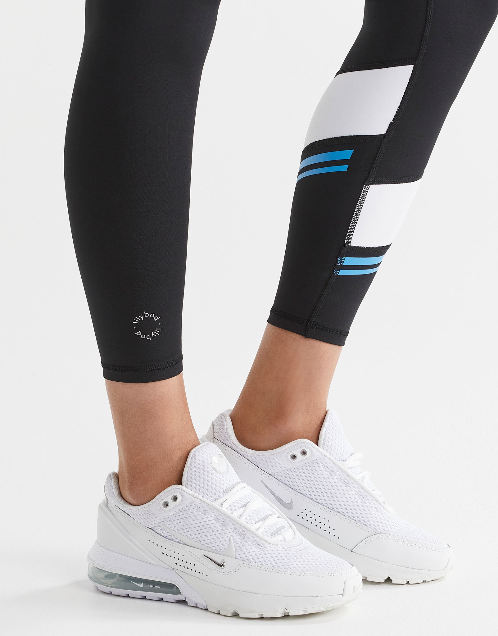 Black leggings with blue stripes worn by a person, paired with white sneakers on a light gray background