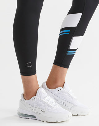 Black leggings with blue stripes worn by a person, paired with white sneakers on a light gray background