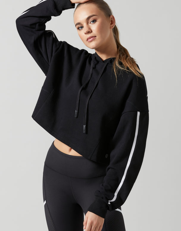 A female model wearing a smoke black oversized hoodie sweater with white printed sleeve hits and a drawcord hood.