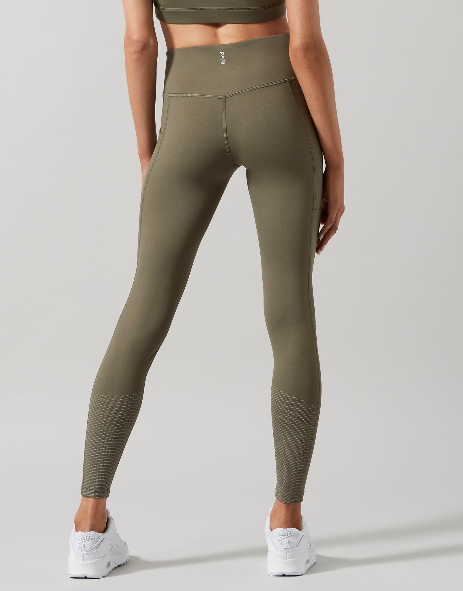 A model wearing high-waist full length khaki leggings with a Lilybod signature sculpting fabric.