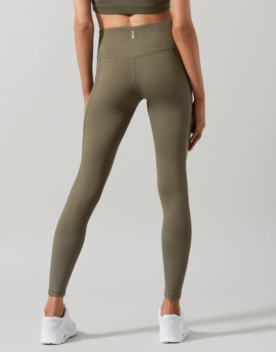 A model wearing high-waist full length khaki leggings with a Lilybod signature sculpting fabric.