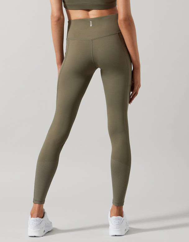 A model wearing high-waist full length khaki leggings with a Lilybod signature sculpting fabric.
