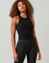 Woman wearing a black sleeveless top and leggings against a plain background