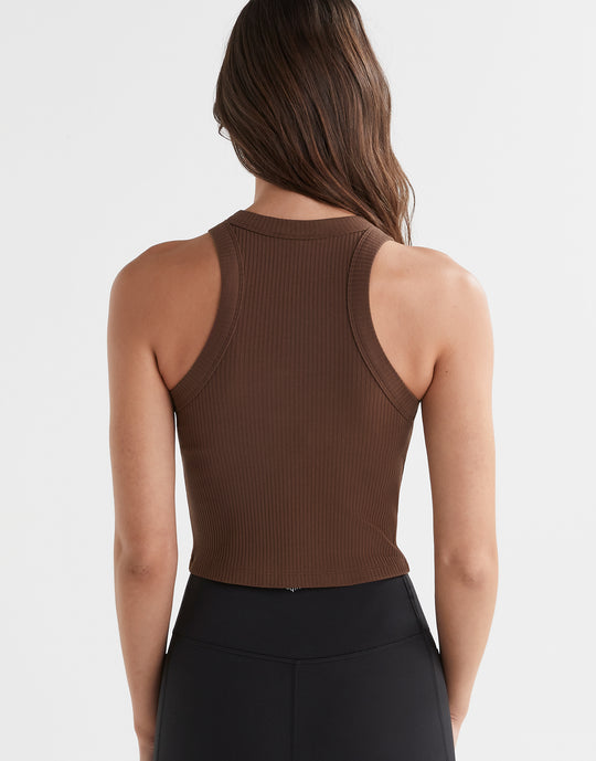 A  model wearing a brown Lilybod Harmony Tank Top in a slim-fit design, paired with black leggings.