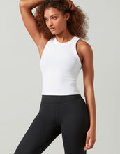 Woman wearing a white sleeveless top and black leggings against a light gray background