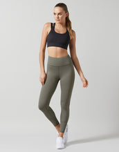 Woman wearing a black sports bra and green leggings on a white background