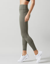 Person wearing olive green leggings and white sneakers on a light gray background