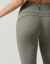 Close-up of a person wearing olive green leggings with a visible brand logo on a light gray background