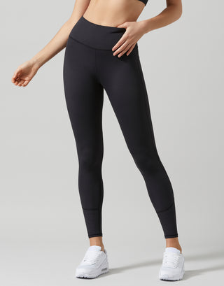 A model wearing black high-waisted athletic leggings and white sneakers, shown from the waist down against a light gray studio background.