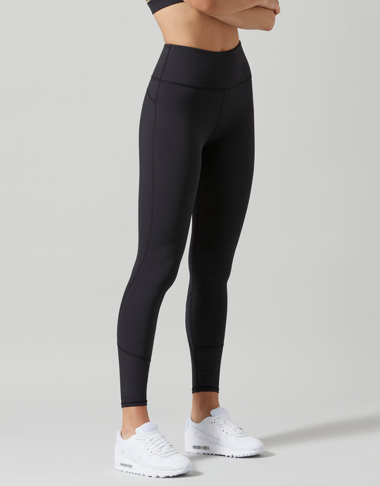 A model wearing high-waisted black athletic leggings and white sneakers, shown from the waist down against a light gray studio background.