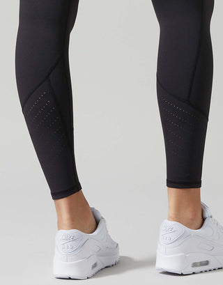 Black athletic leggings worn by a model, paired with white Nike Air Max sneakers, shown from the calves down against a light gray studio background.