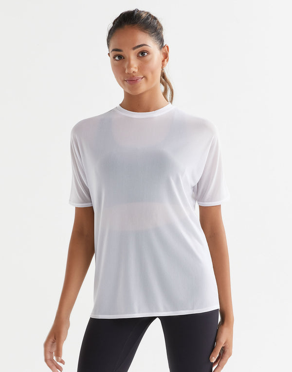 A model wearing a white t-shirt with short sleeves, made from a sheer mesh fabric, standing against a plain background.