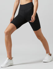 Person wearing black athletic shorts and white sneakers on a light gray background