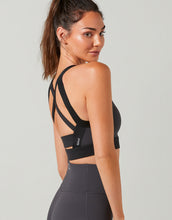 Woman wearing a black sports bra with cut-out design on a gray background