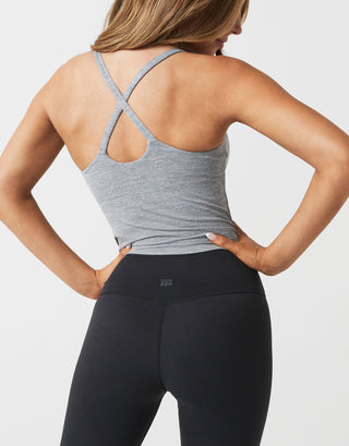 A woman wearing black leggings and a grey tank on a white background.