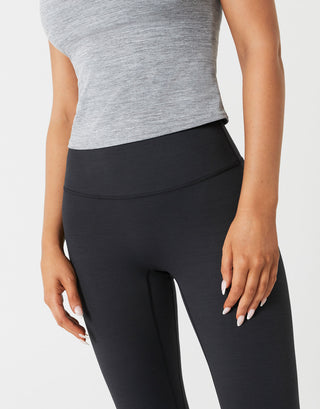Person wearing black leggings and a gray top on a light gray background