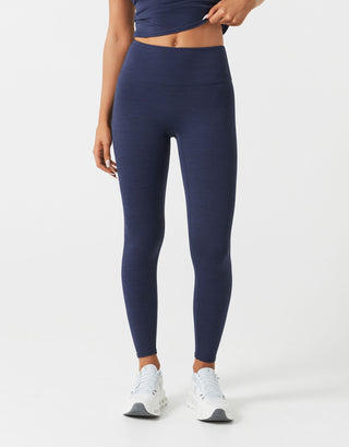 A woman wearing navy blue leggings and white runners on a white background.