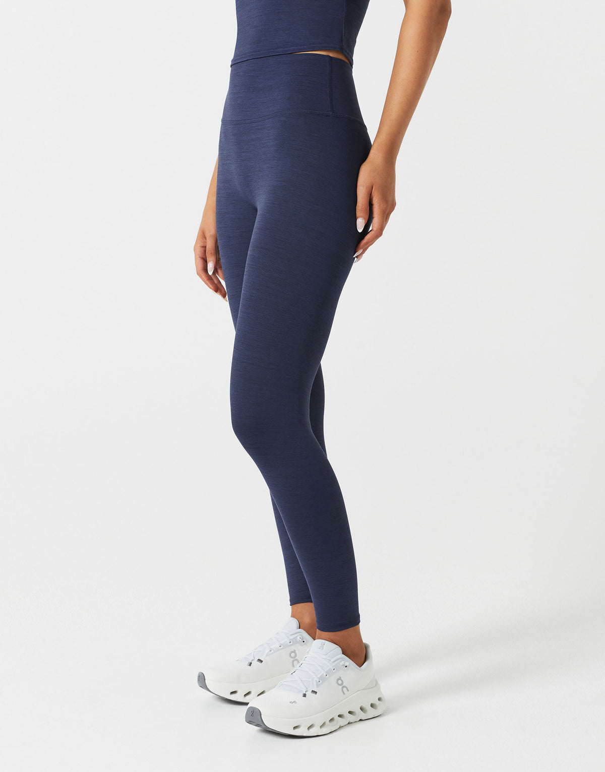 Person wearing navy leggings and white sneakers on a light gray background