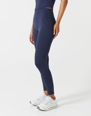 Person wearing navy leggings and white sneakers on a light gray background