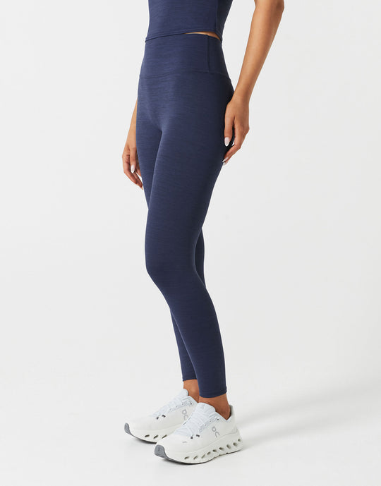 Person wearing navy leggings and white sneakers on a light gray background