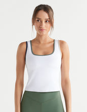 Woman wearing a white tank top with green trim and green leggings on a light gray background