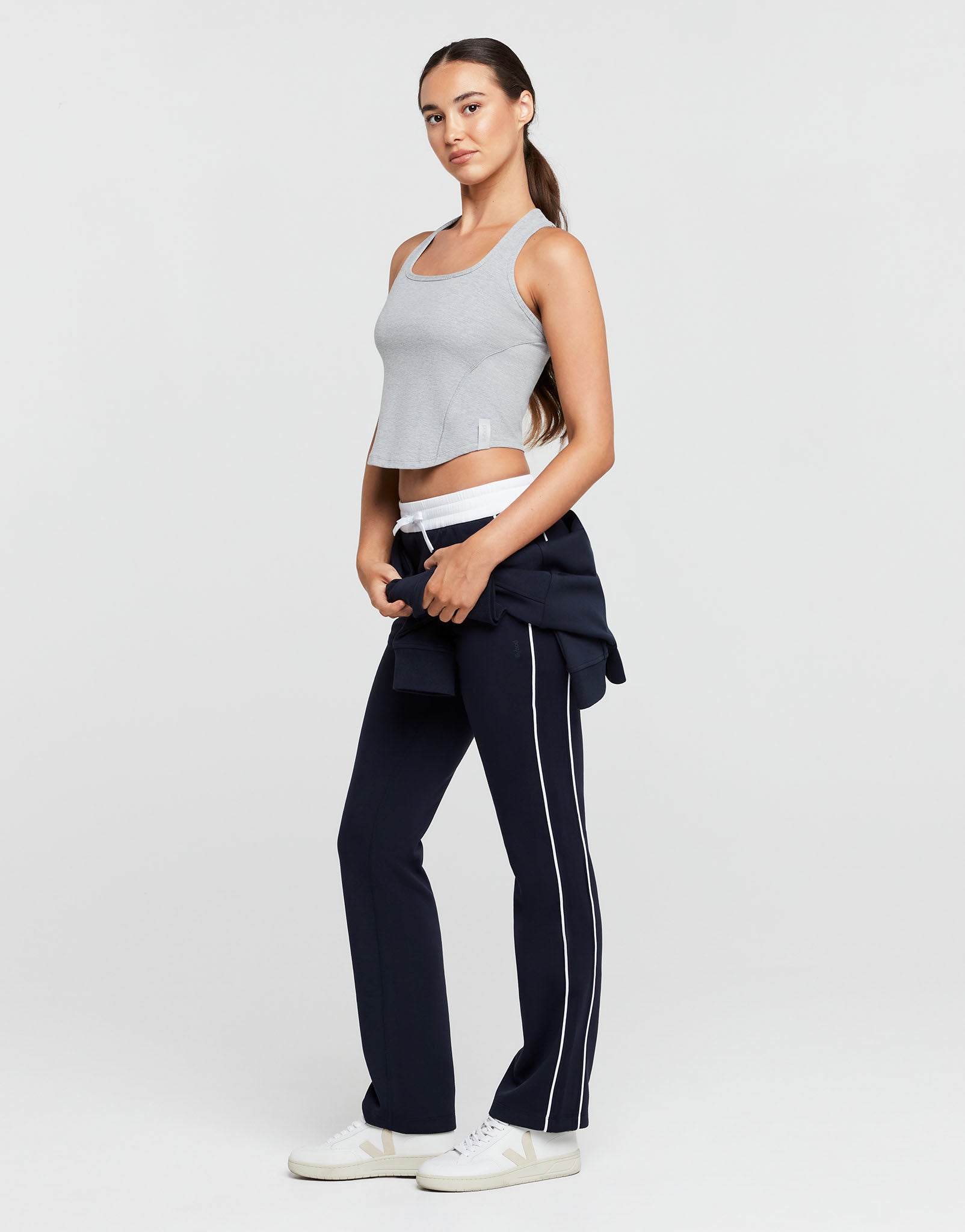 Woman wearing a gray crop top and navy pants with a white stripe on a light gray background