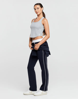 Woman wearing a gray crop top and navy pants with a white stripe on a light gray background