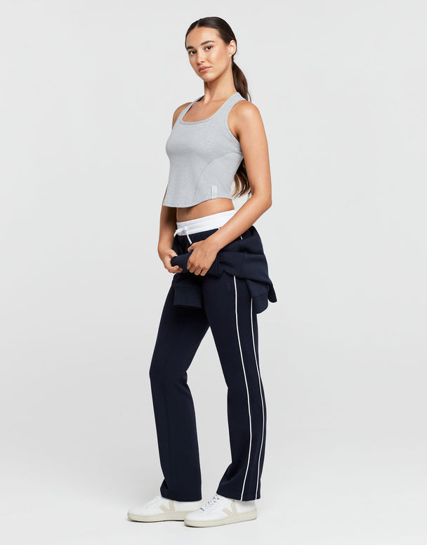 Woman wearing a gray crop top and navy pants with a white stripe on a light gray background