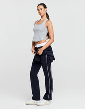 Woman wearing a gray crop top and navy pants with a white stripe on a light gray background