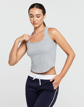 Woman wearing a gray tank top and navy pants on a light gray background