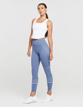 Woman wearing a white sleeveless top and blue leggings on a white background