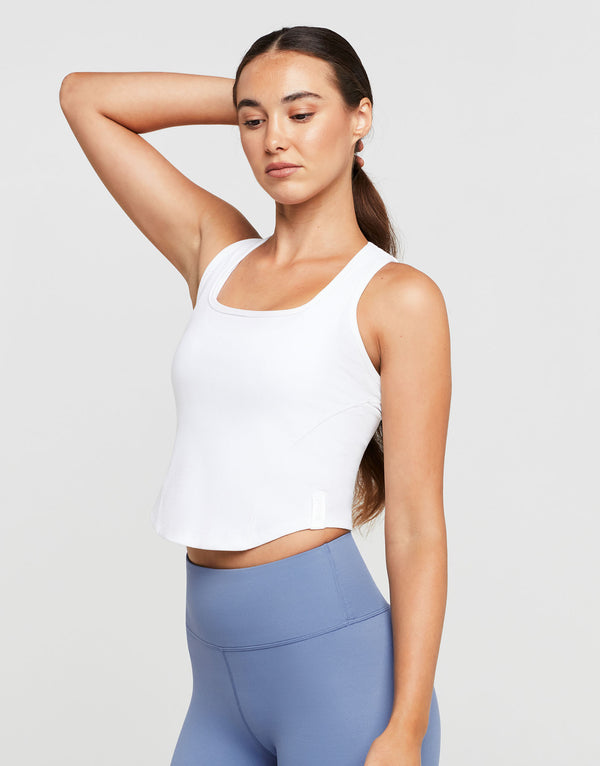 Woman wearing a white tank top and blue leggings on a light gray background